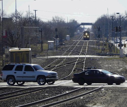 Train driving down tracks going to probably hit a car